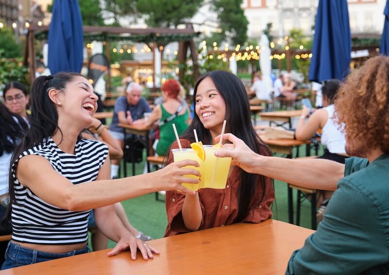 Freunde stoßen beim Sommerfest im Freien auf Getränke an, lachen und genießen die gemeinsame Zeit