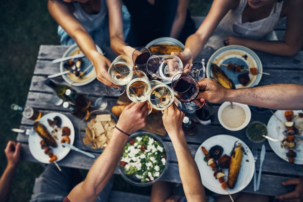Gruppe von Menschen stößt über einem Tisch mit Wein an.